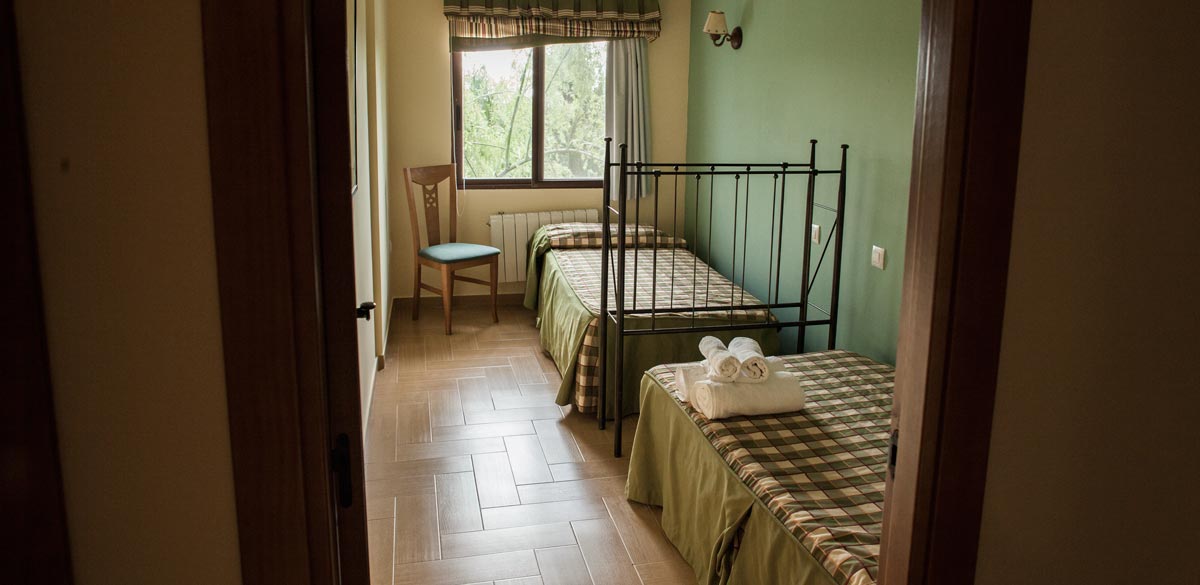 Una habitación de un apartamento del Complejo Rural Puerto Mágina. Dispone de dos camas de 90 y cabeceros de forja. Habitación con decoración en tonos verdosos.