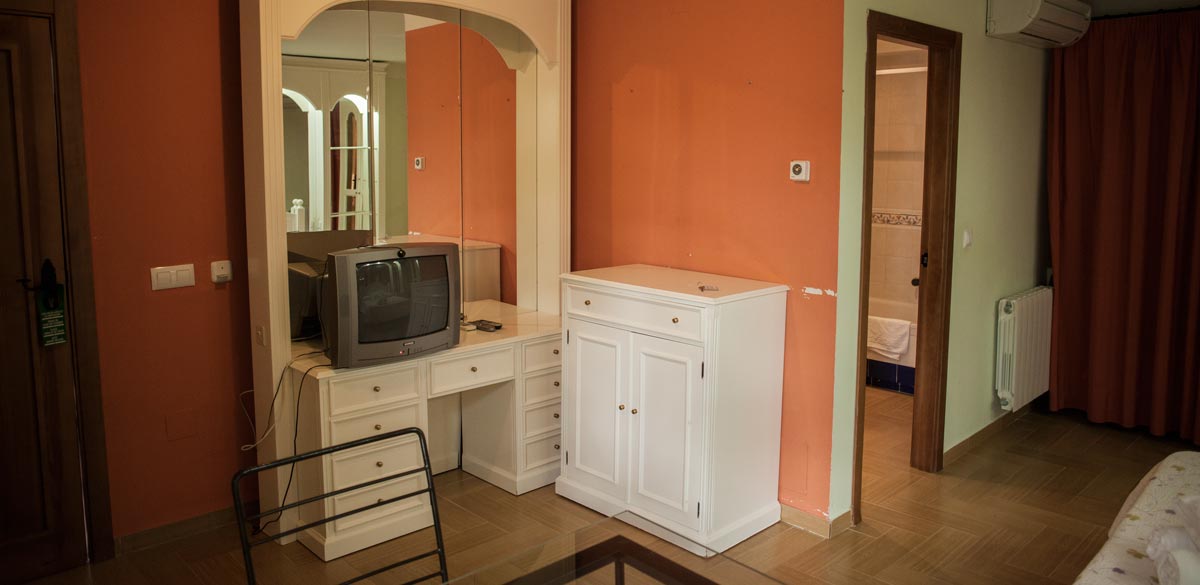 Mueble aparador y tocador blanco con un gran espejo y una televisión, de una de las habitaciones del Complejo Rural Puerto Mágina.