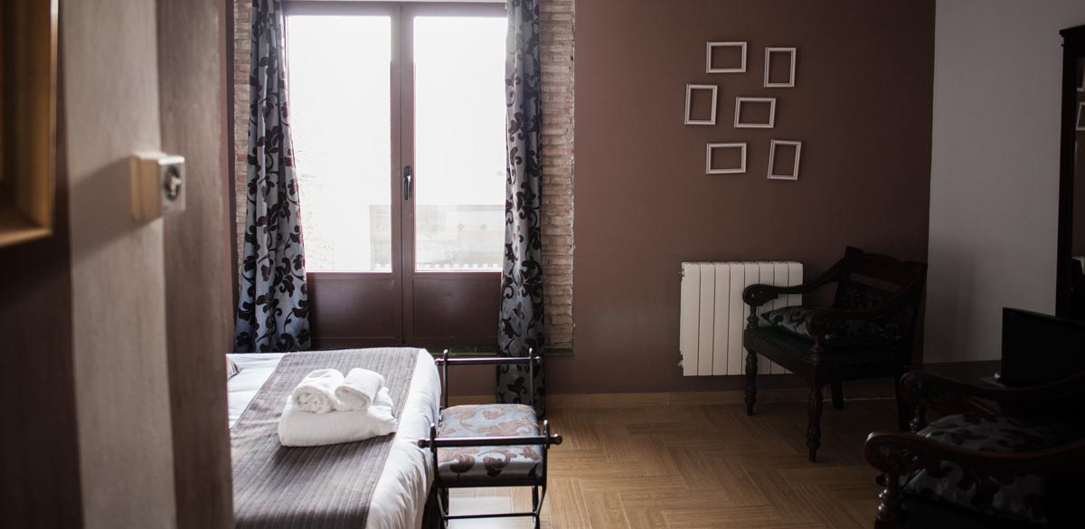 Detalles de una de las habitaciones, con tonos marrones, del Complejo Rural Puerto Mágina. Se muestra el acceso a una terraza exterior.